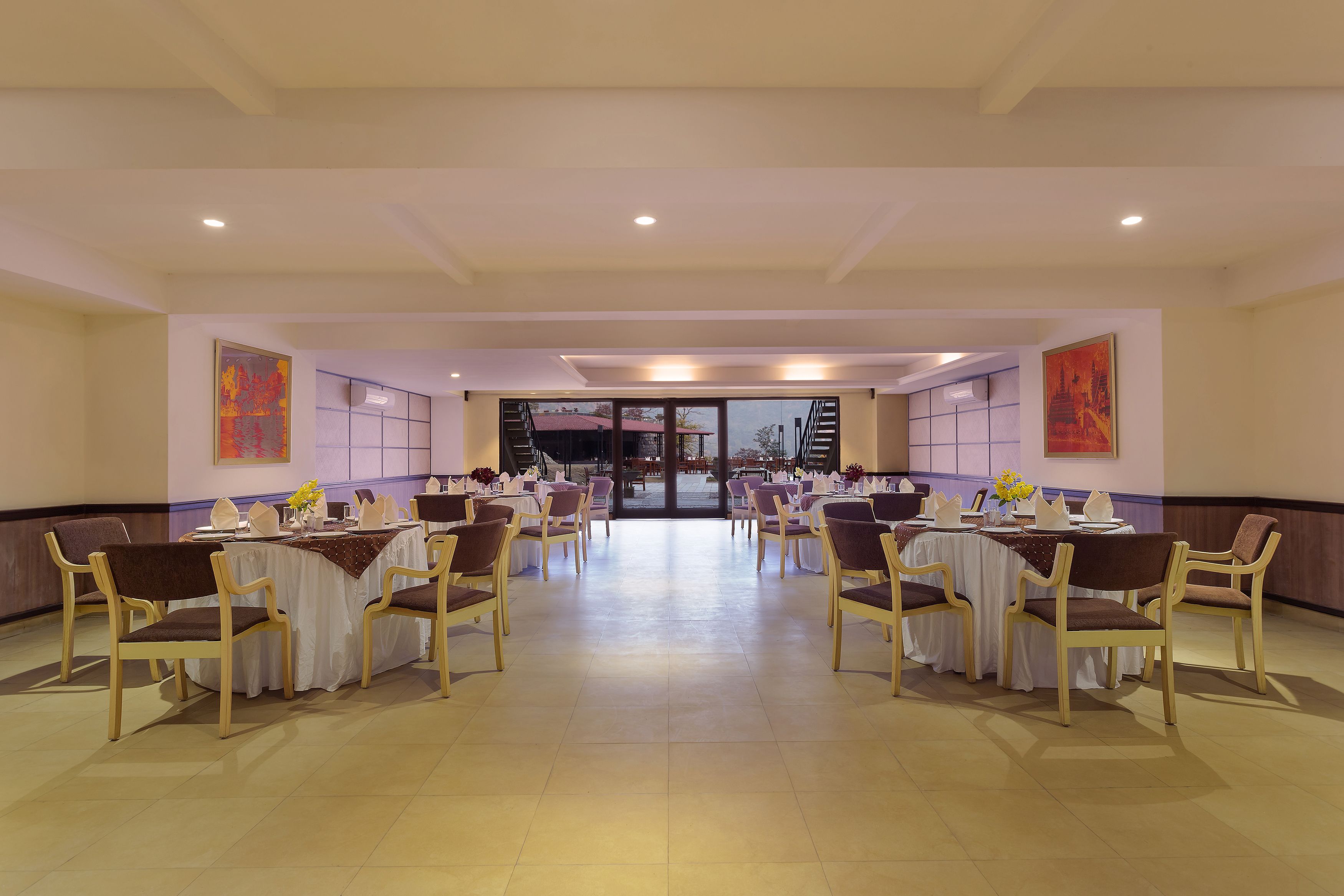 A spacious banquet hall with multiple round tables and chairs, large windows, and a view of the outside.