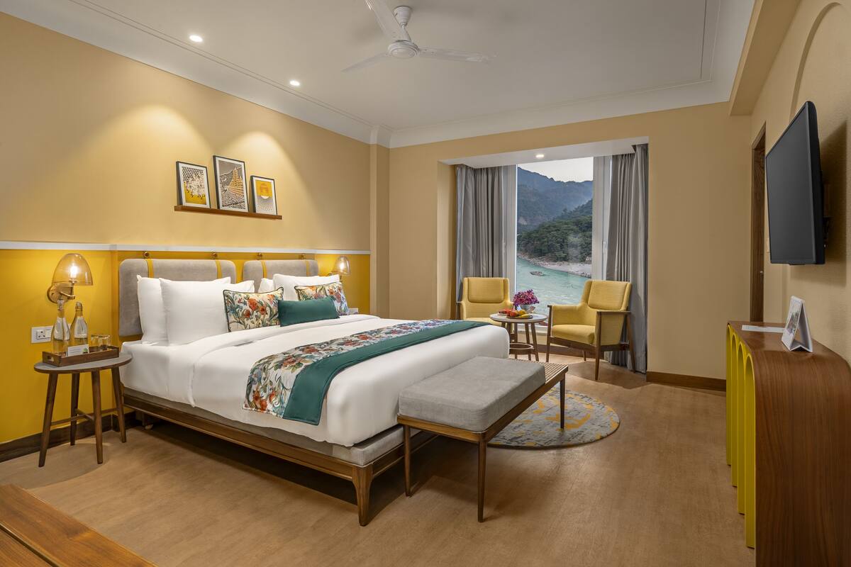 Quarto de hotel com cama, mesas de cabeceira, escrivaninha, cadeira, televisão e vista para o mar.