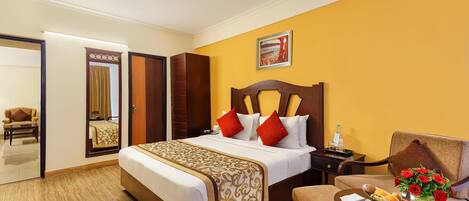 A hotel room with a large bed, a bedside table with a vase of flowers, a chair, and a small table with breakfast items.