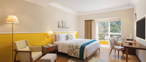 Habitación de hotel con cama, escritorio, silla, lámpara y vista al exterior.