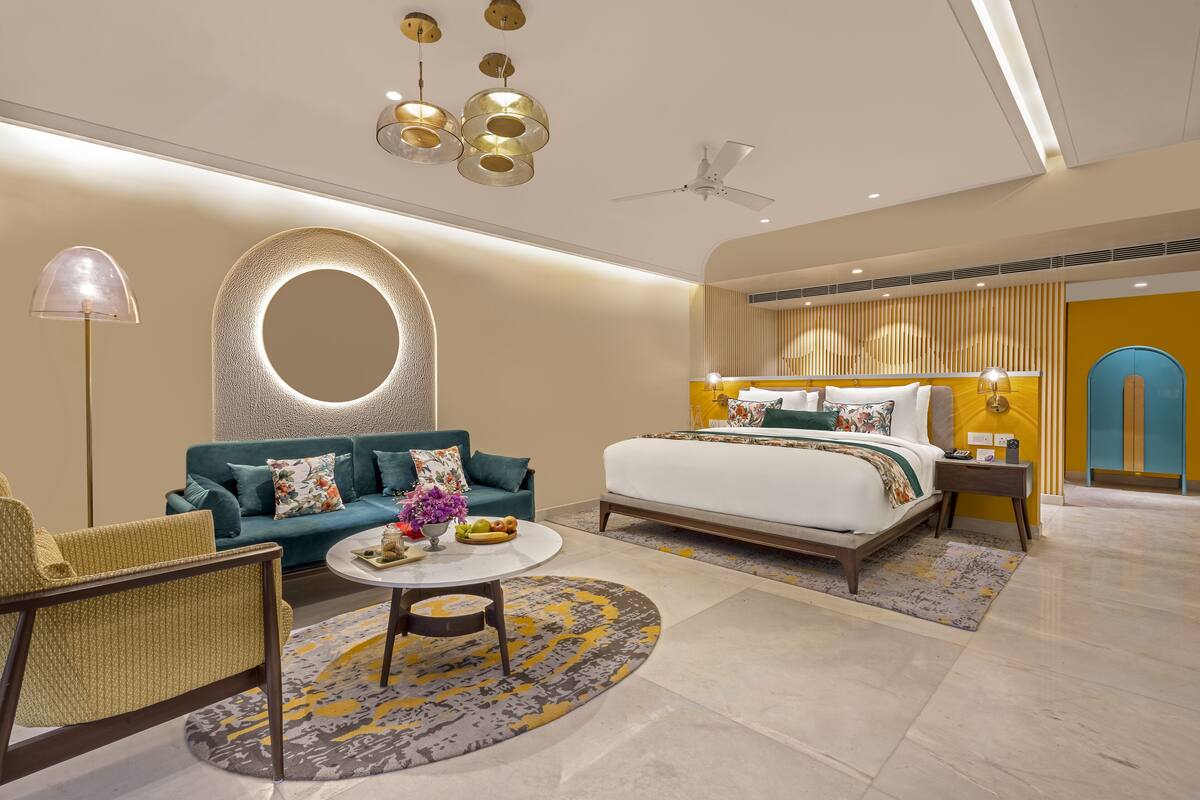 Quarto de hotel moderno com uma cama, sofá e uma mesa de centro redonda.