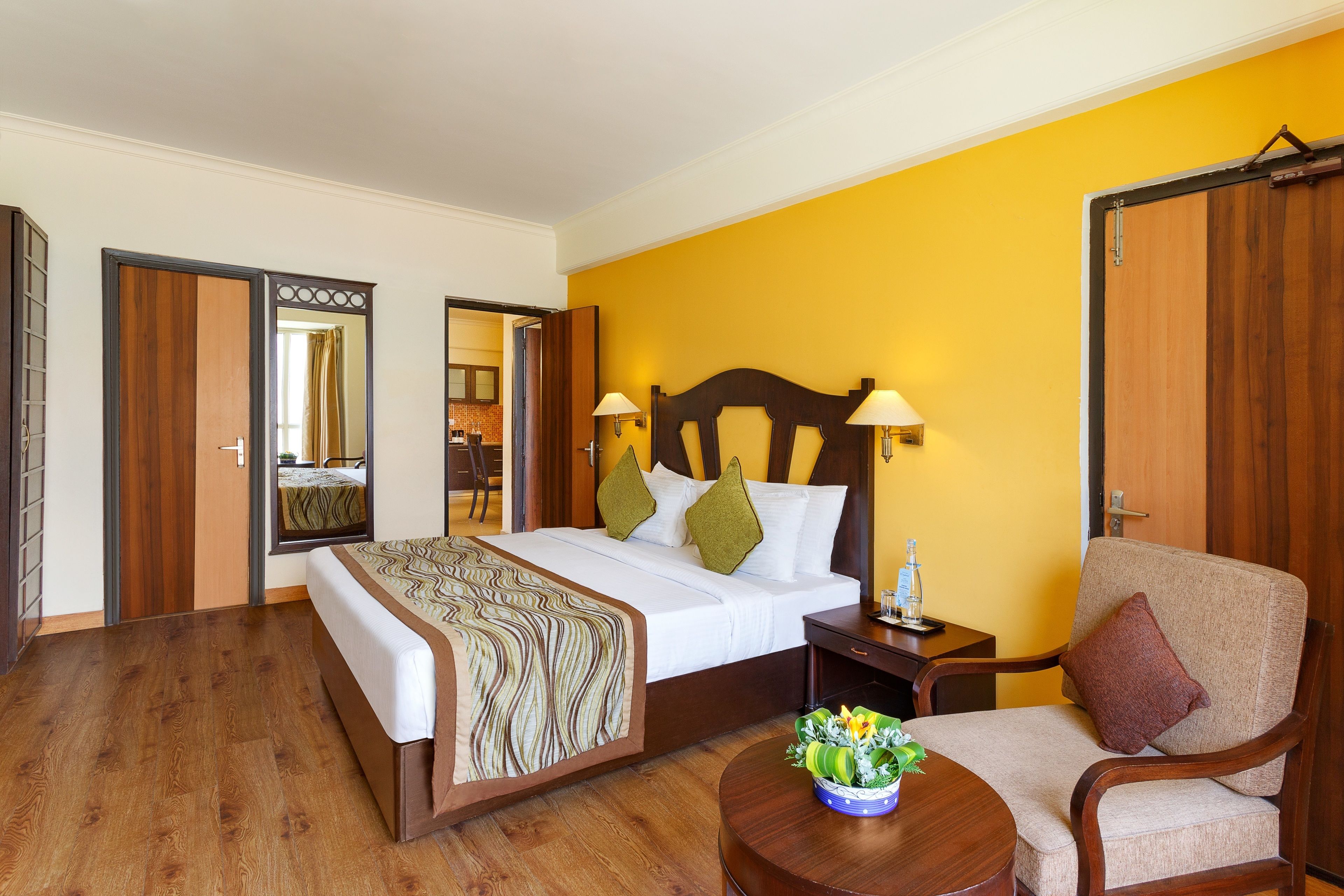 A hotel room with a bed, bedside table, chair, and a small table with a vase of flowers.