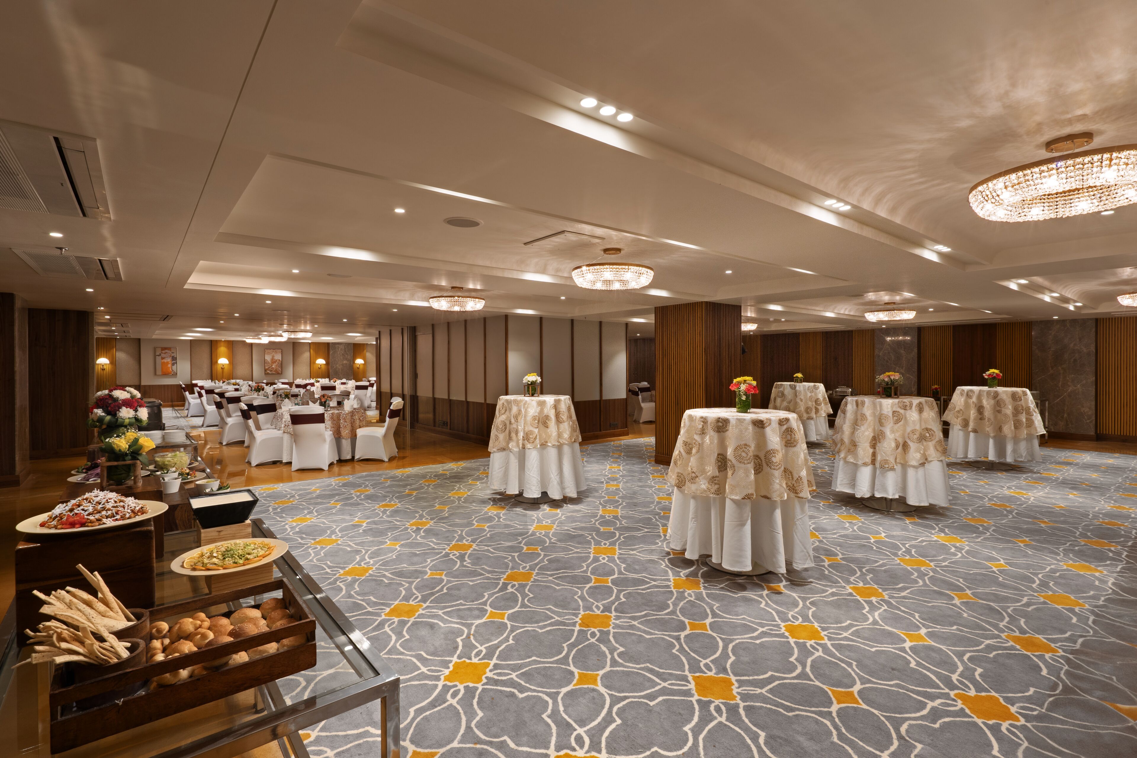Un salón de banquetes con mesas dispuestas para un evento formal, con alfombra estampada y elegantes candelabros.