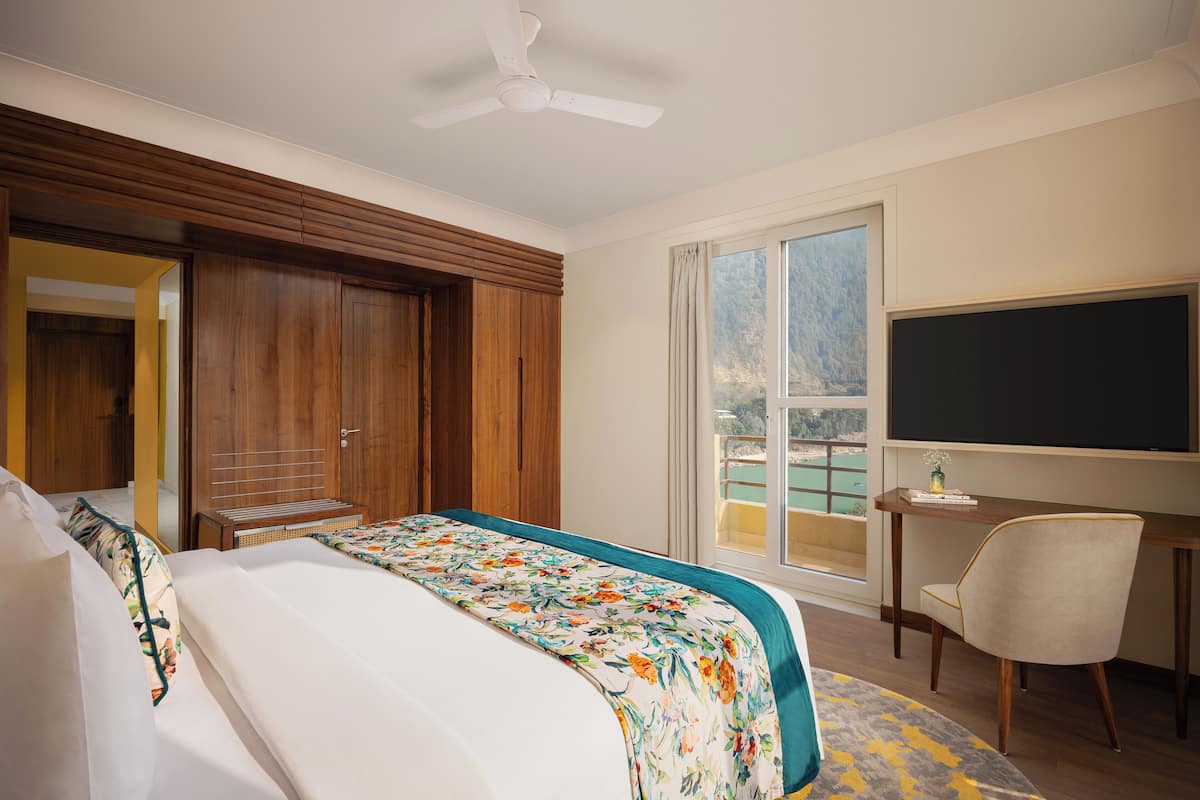 Quarto de hotel com cama, escrivaninha, cadeira, televisão e vista para a varanda.