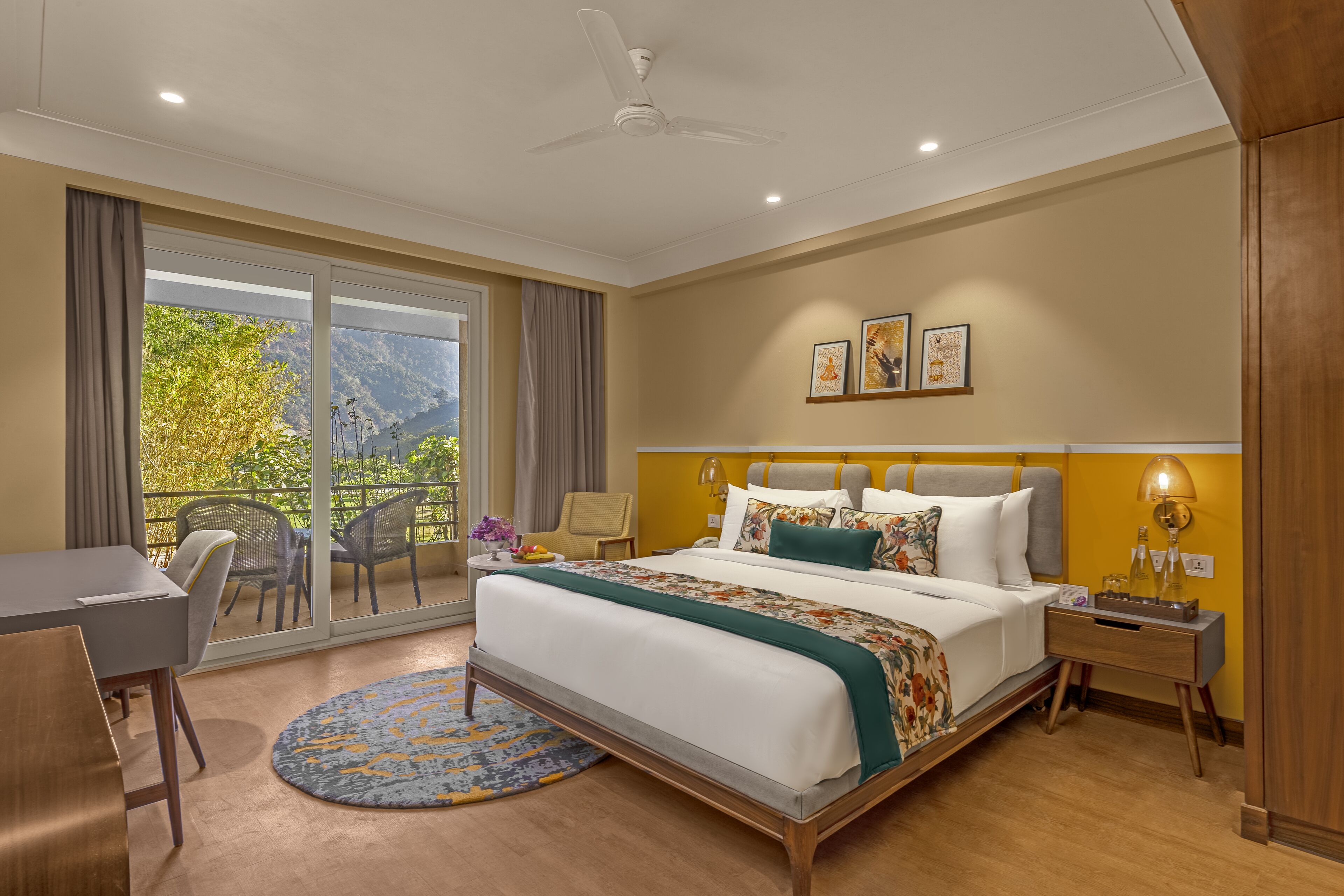 A hotel room with a large bed, a desk, and a balcony with chairs.