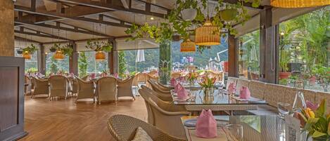 A restaurant with wicker furniture, glass tables, and hanging plants.