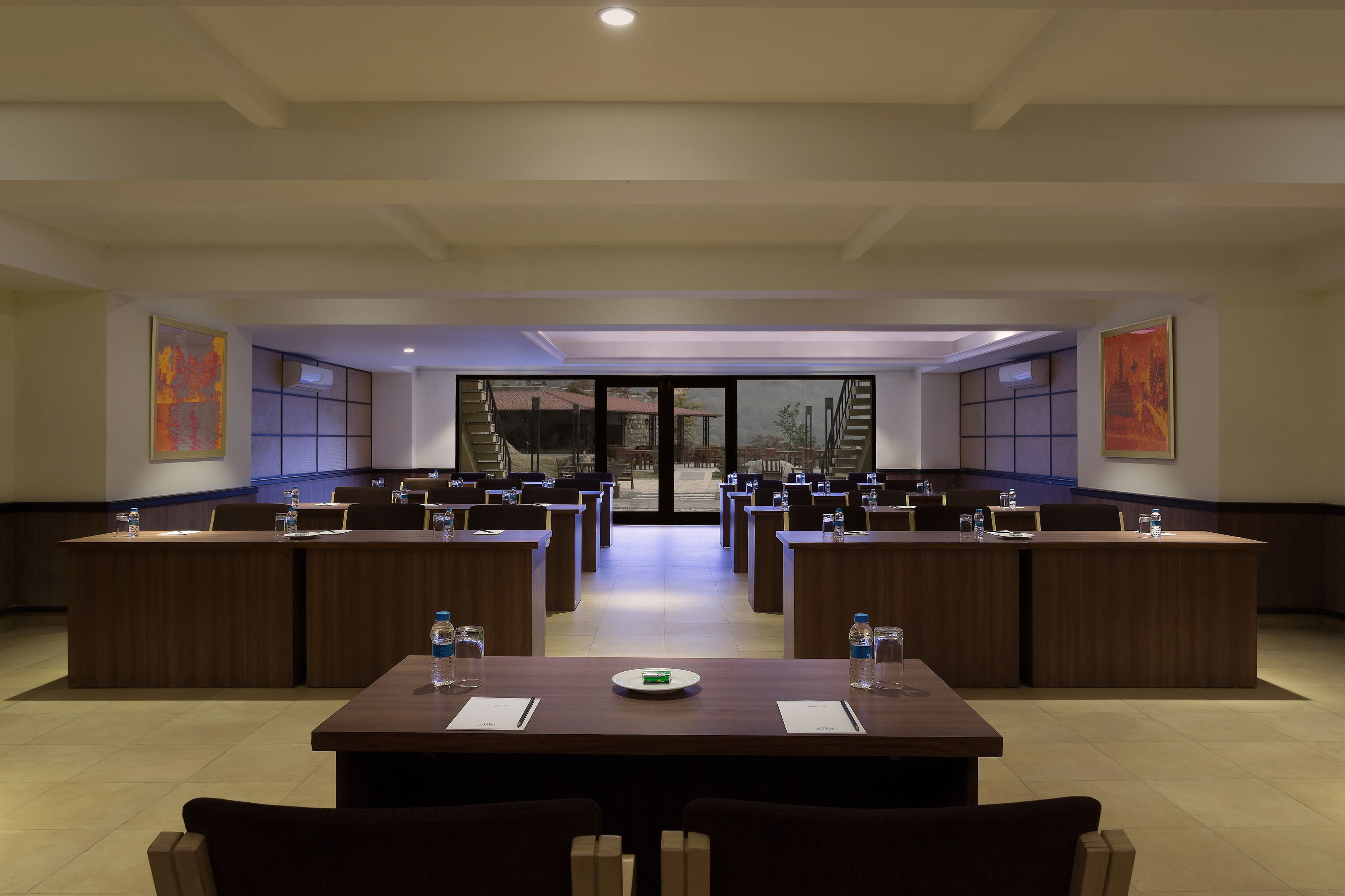 A conference room with multiple tables and chairs, large windows, and artwork on the walls.