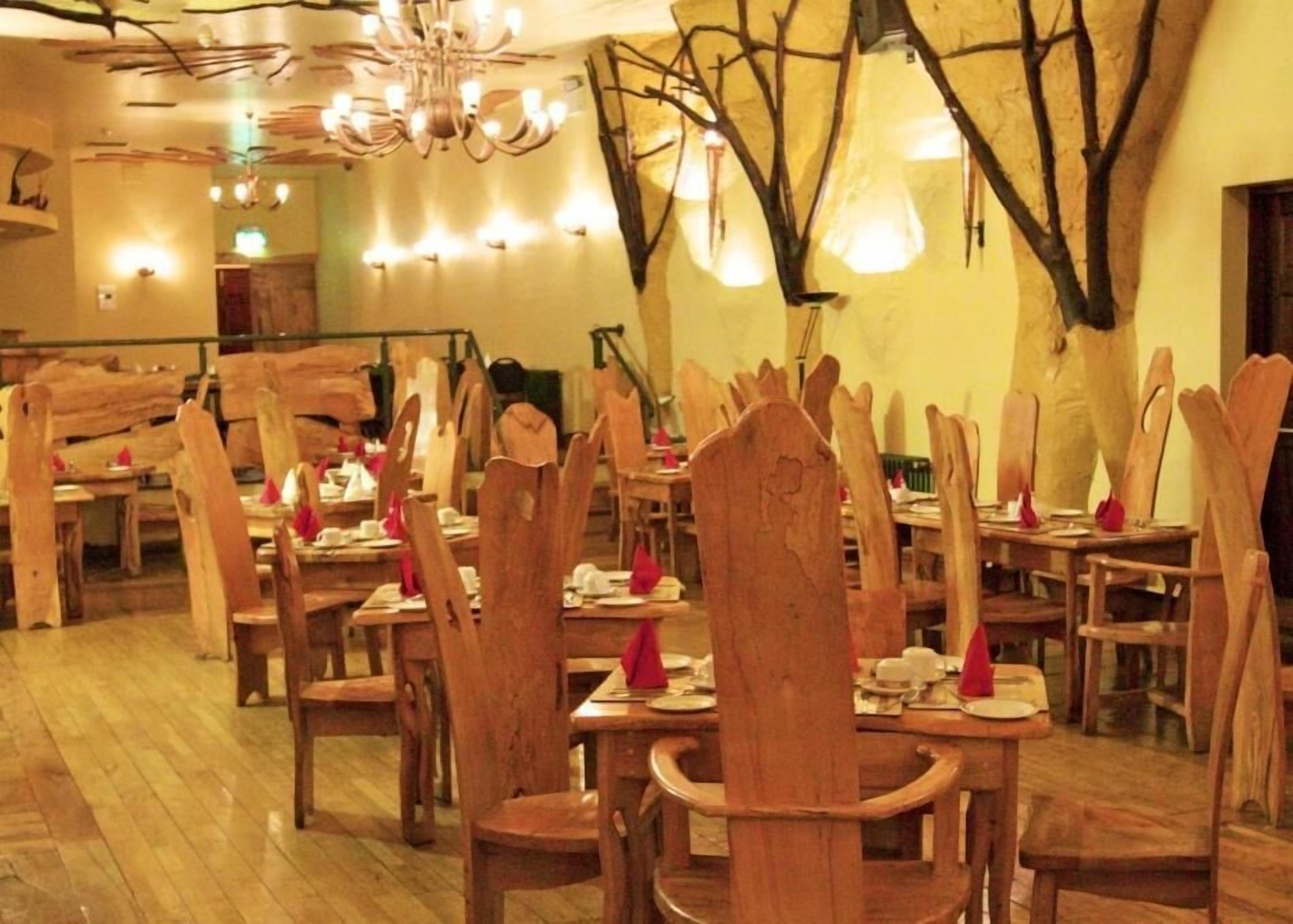 A restaurant with wooden chairs and tables, a chandelier, and wall-mounted lights.