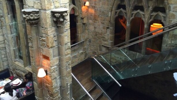 A stone interior with arched windows and a glass railing.