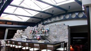 A bar area with a stone wall, multiple bar stools, and a variety of bottles.
