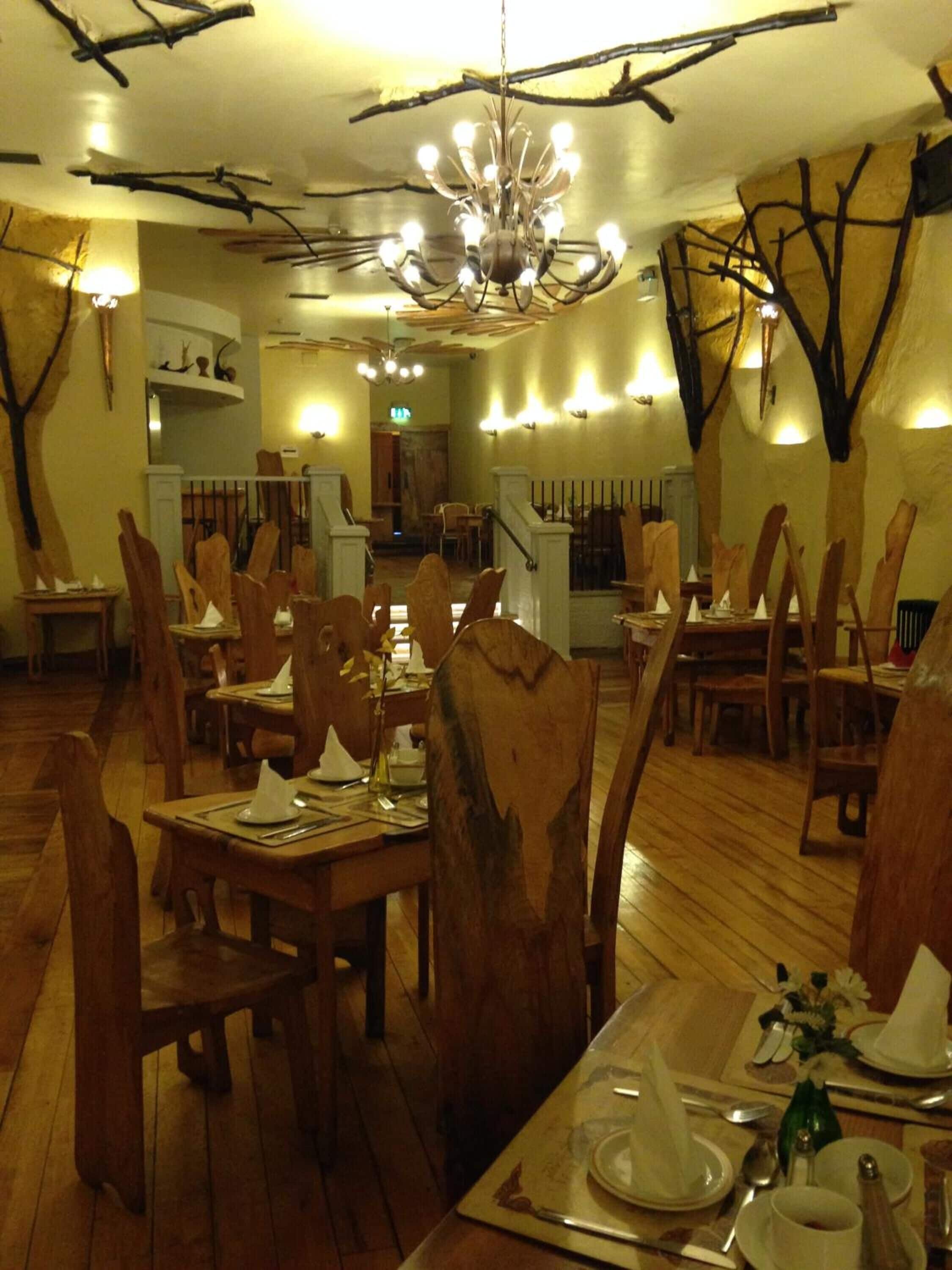 A restaurant with wooden chairs and tables, a chandelier, and wall-mounted lights.