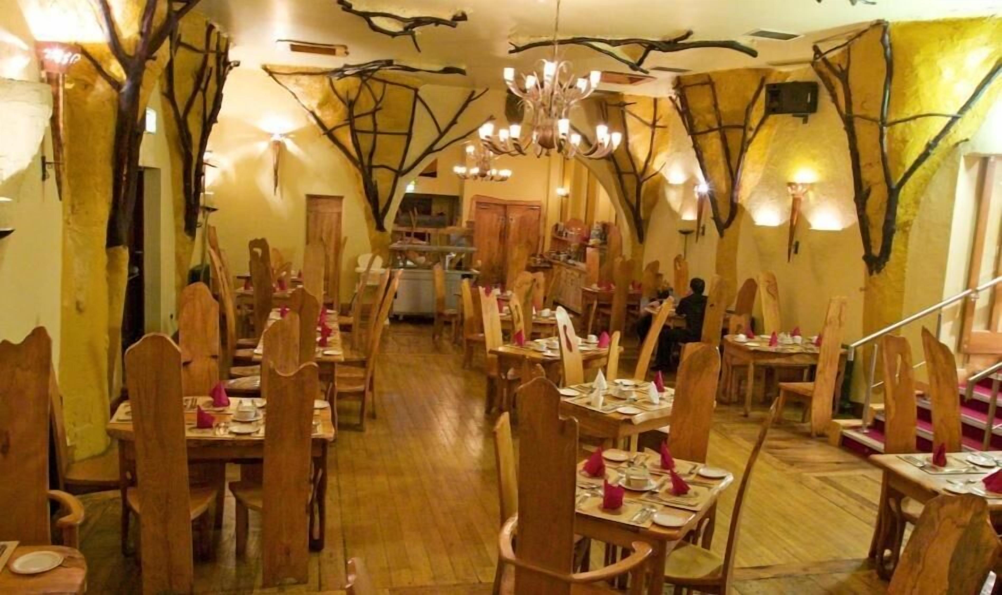 A restaurant with wooden chairs and tables, a chandelier, and wall decorations resembling tree branches.