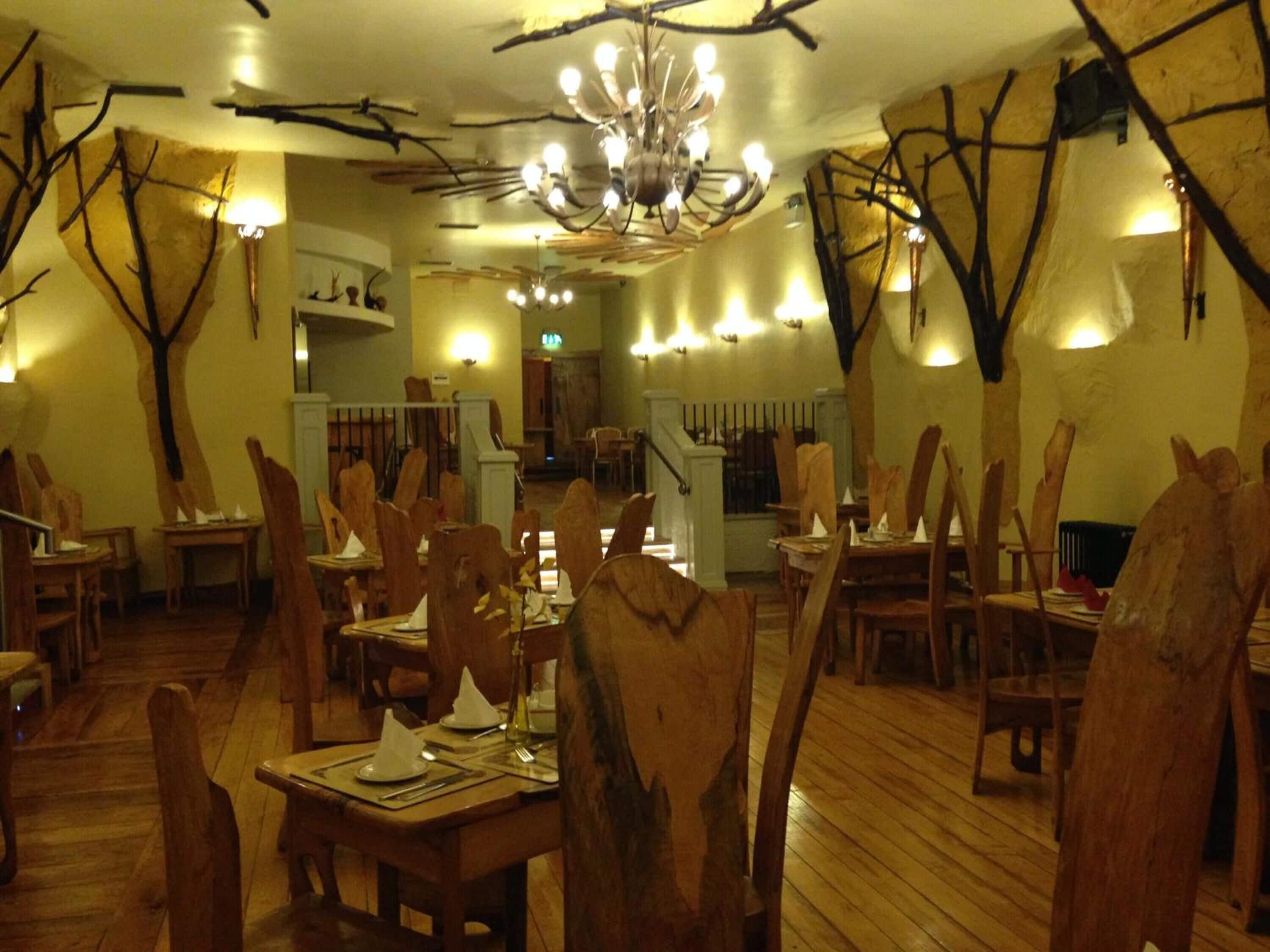 A restaurant interior with wooden chairs and tables, a chandelier, and wall-mounted lights.