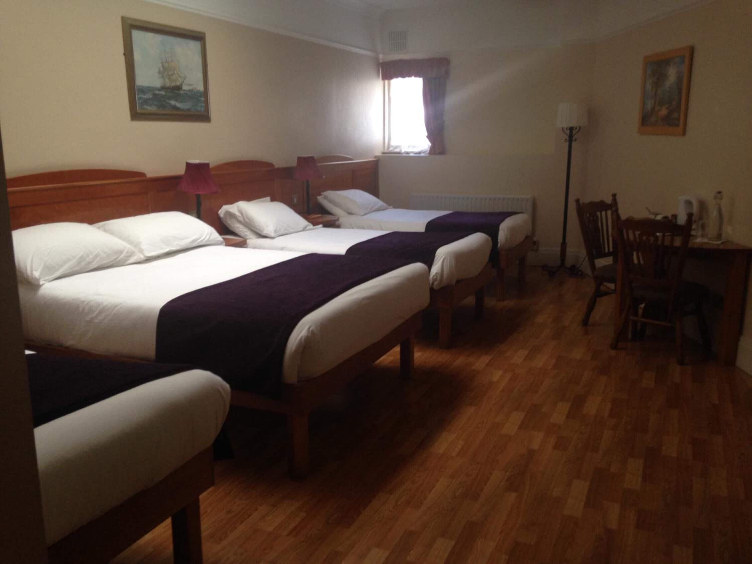Habitación de hotel con dos camas individuales, piso de madera, un escritorio con silla y ventana con cortinas.
