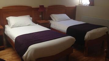 A hotel room with two single beds, wooden headboards, a nightstand with a lamp, and a window with curtains.