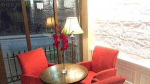 A room with a round table and two red chairs, a vase with red flowers, and a lamp.