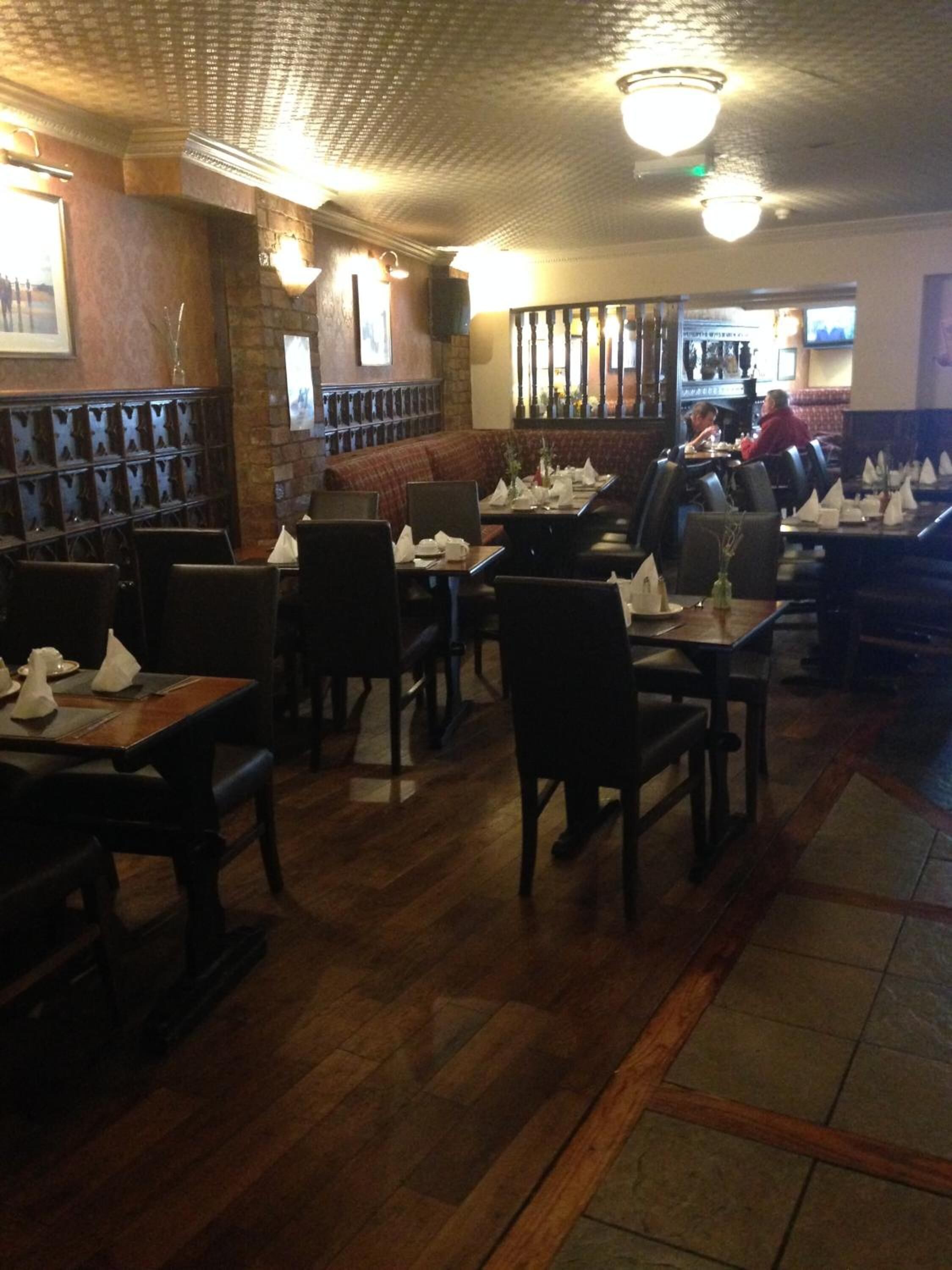 A restaurant interior with wooden flooring, tables with chairs, and a bar area.