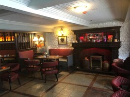 A cozy pub with red upholstered seating, a bar area with bottles, and a fireplace.
