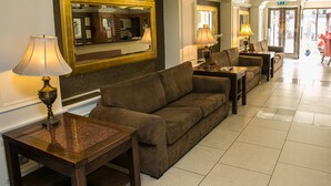 A hotel lobby with a brown sofa, two tables with lamps, a large mirror, and a tiled floor.