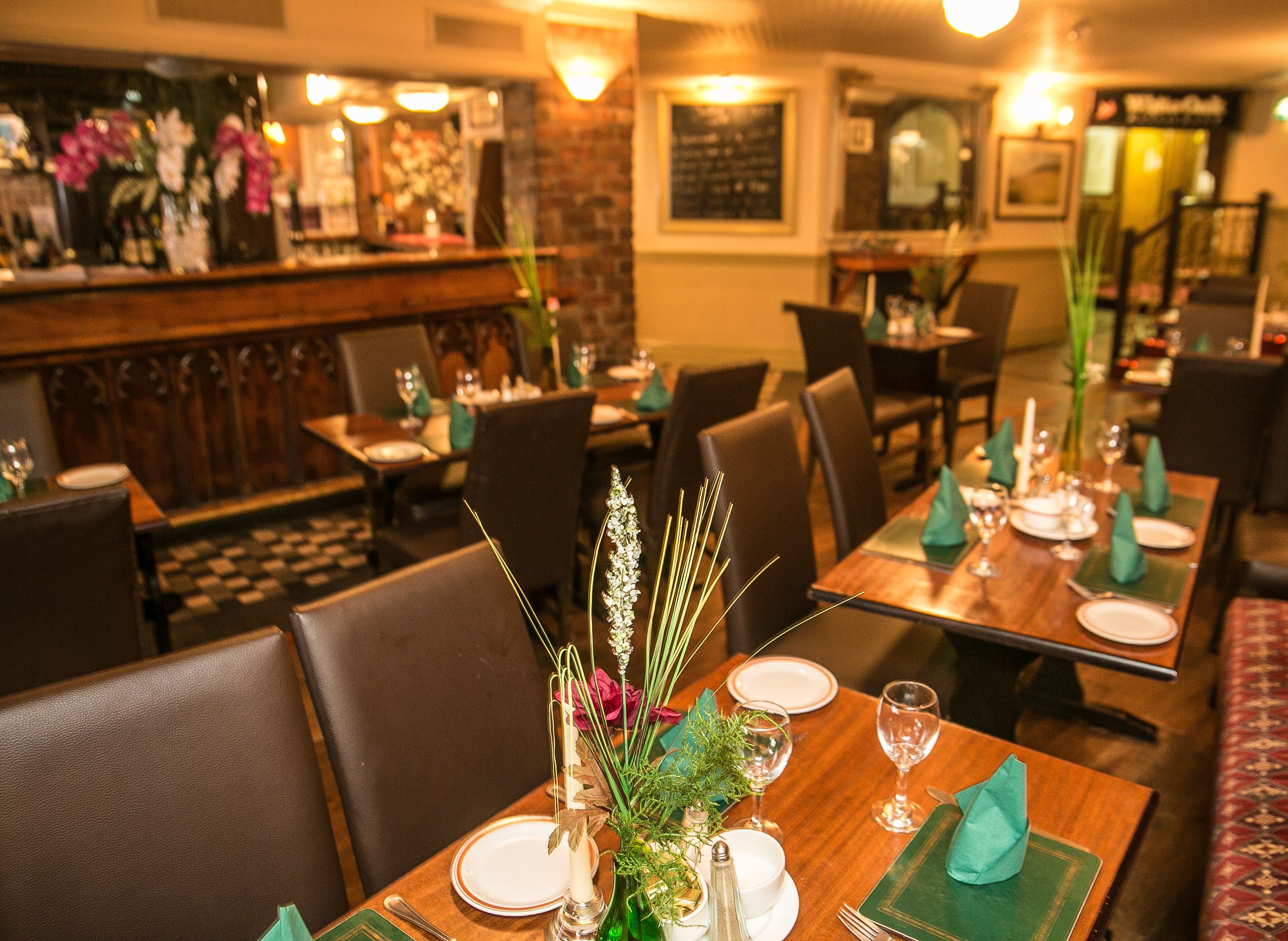 A restaurant interior with wooden tables set for dining, chairs, and a bar area with a menu board.