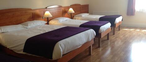 Une chambre d’hôtel avec quatre lits en bois, chacun doté d’une tête de lit et de lampes de chevet.