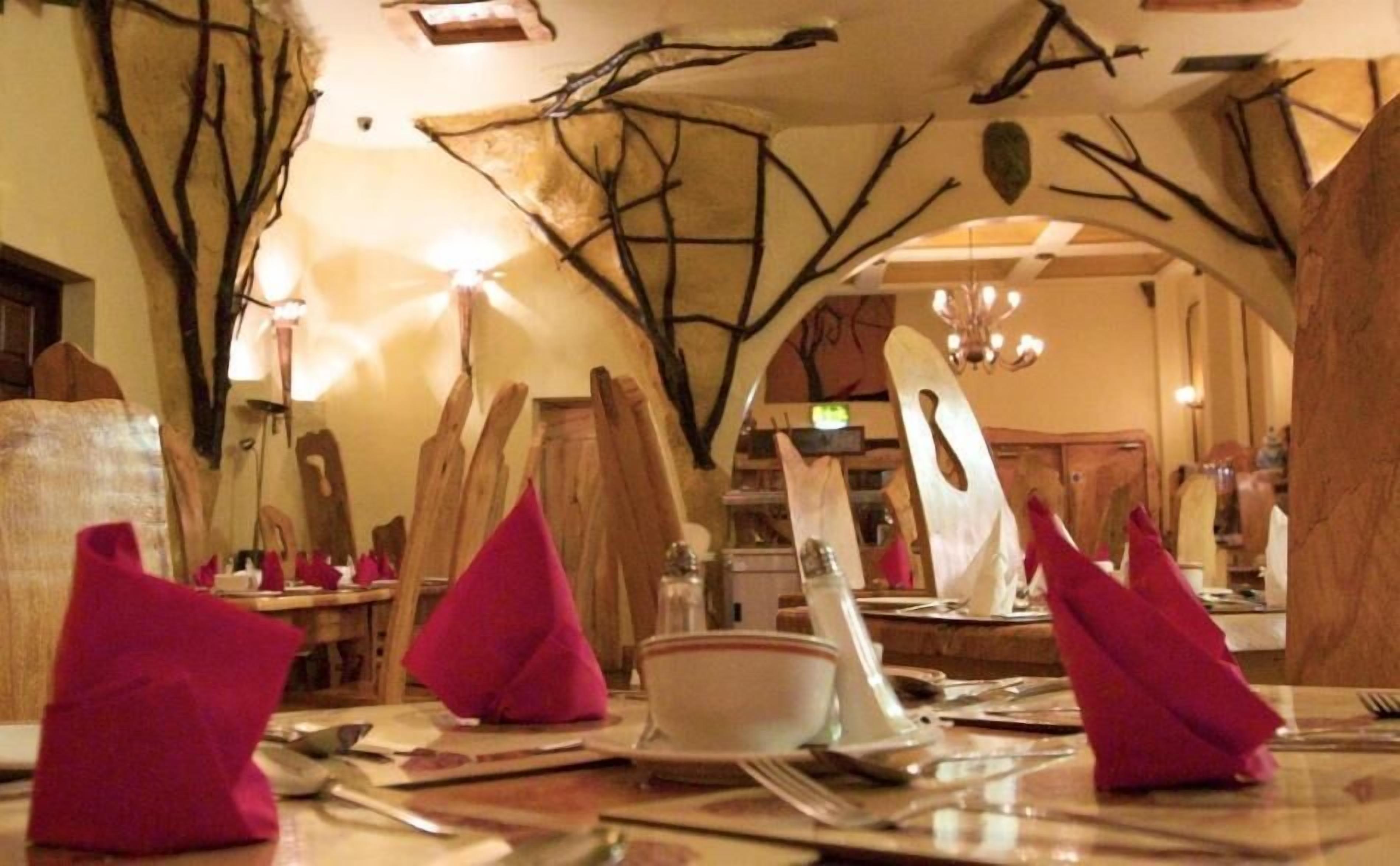 A restaurant interior with high wooden beams and a chandelier. Tables are set with pink napkins and silverware.
