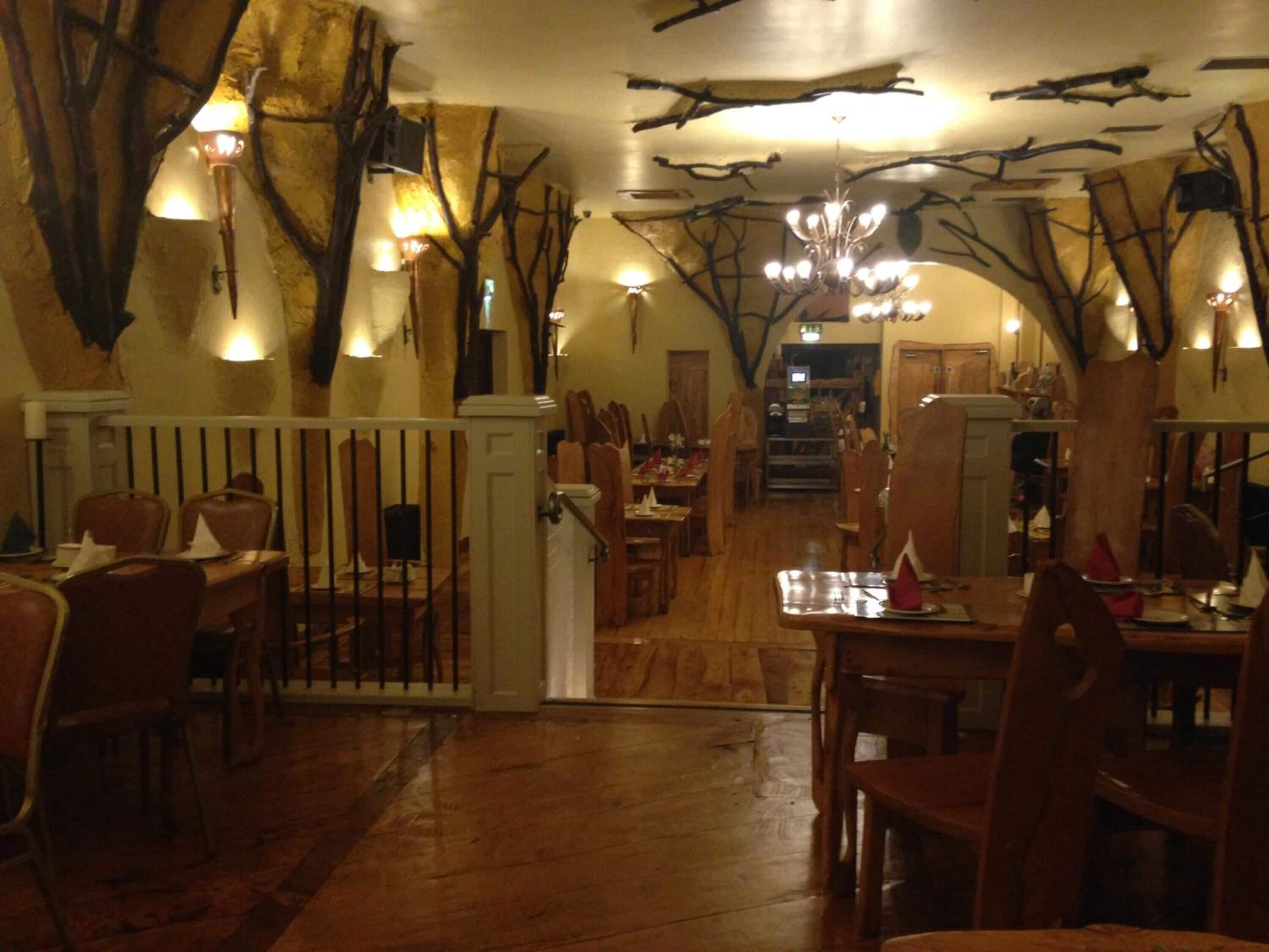 Un restaurante con suelo de madera, un área central de comedor con mesas y sillas, y un techo decorado con ramas y luces.
