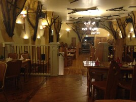 Un restaurante con suelo de madera, un área central de comedor con mesas y sillas, y un techo decorado con ramas y luces.