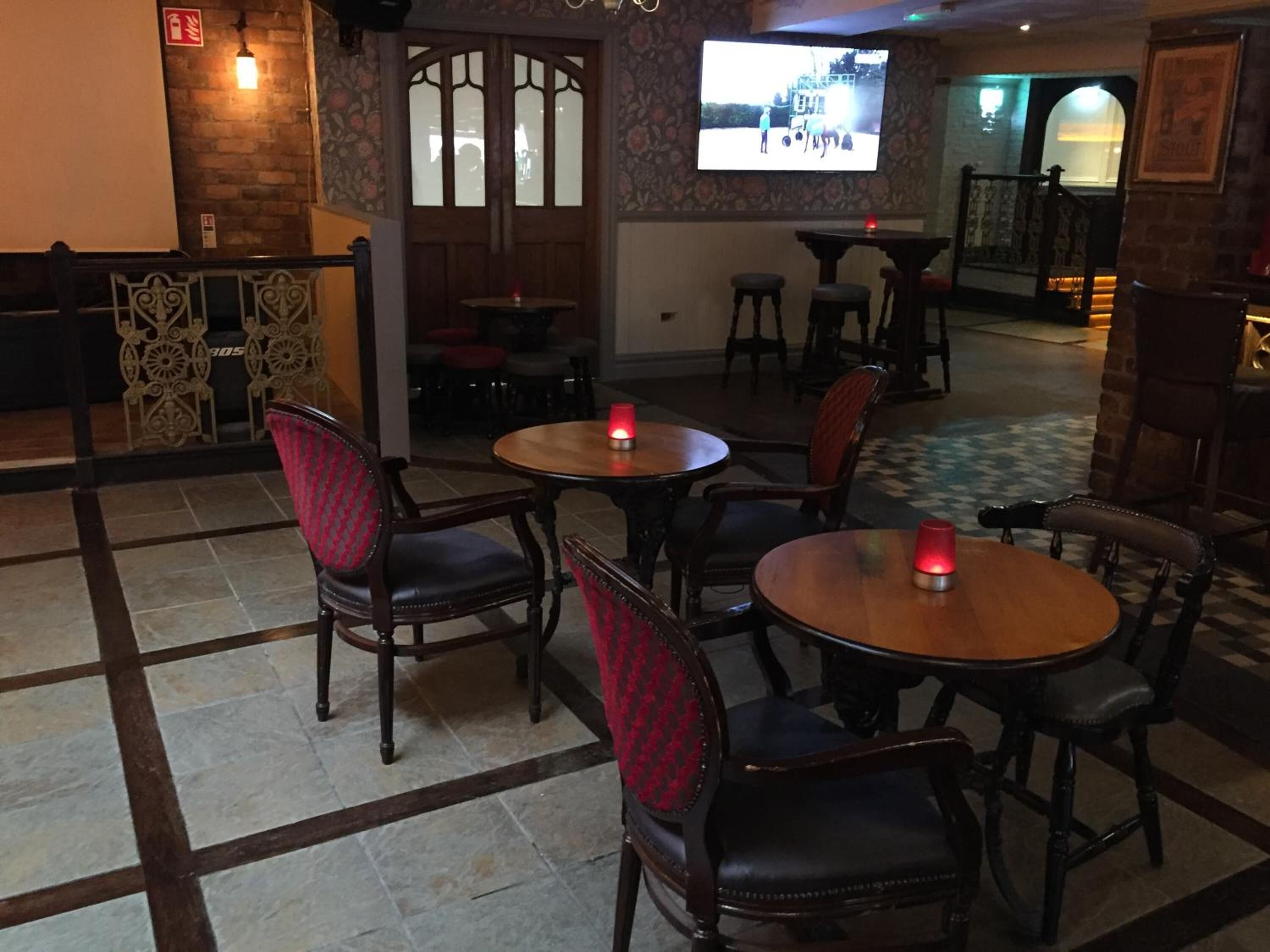 Een restaurantinterieur met houten tafels en stoelen, een bar en een televisiescherm waarop een scène te zien is.
