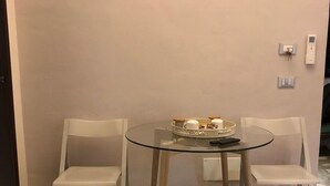 Una habitación pequeña con una mesa de vidrio y dos sillas blancas, un interruptor de luz y un termostato en la pared.