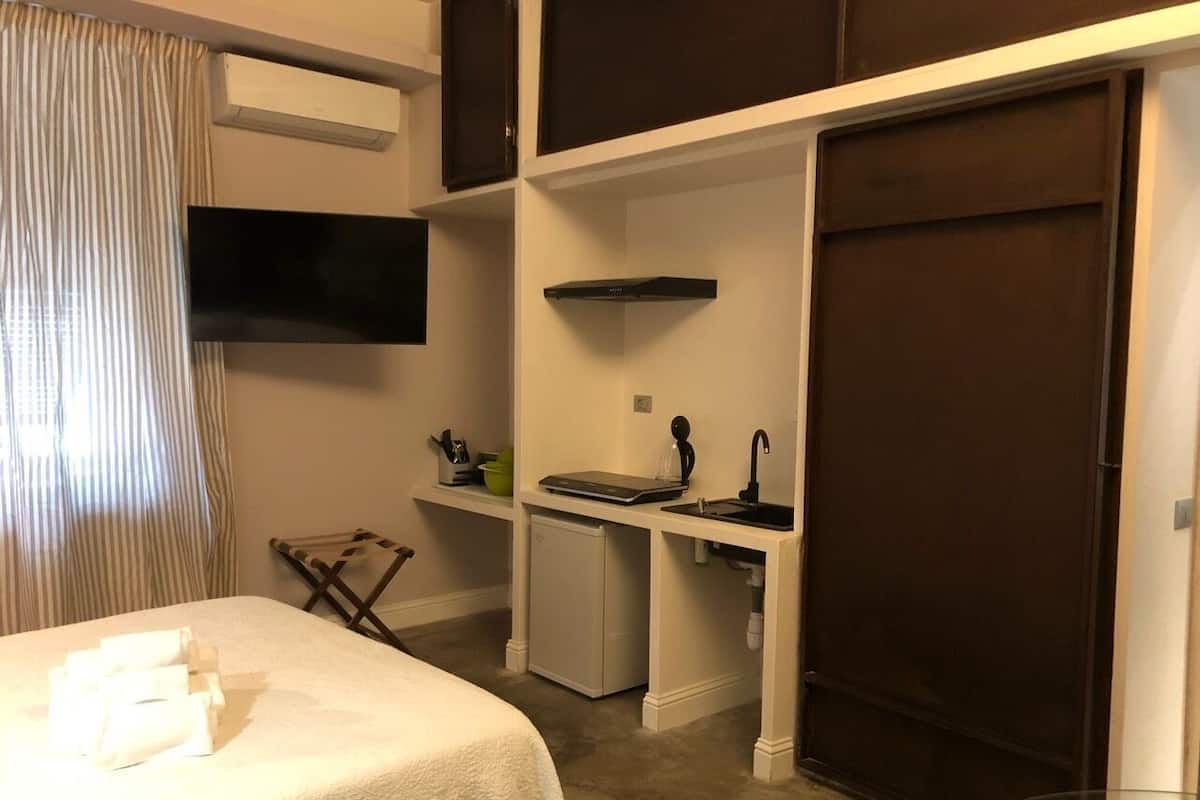 Une chambre d’hôtel de taille réduite, comprenant un lit, une petite kitchenette, une télévision et une armoire.