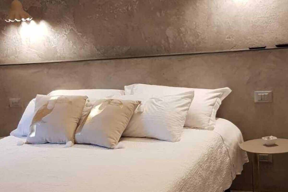 Une chambre à coucher avec un grand lit, du linge de lit blanc et deux lampes suspendues.