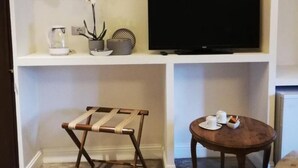 Habitación de hotel con televisión sobre un estante blanco, una mesita con una silla y un tendedero de madera.