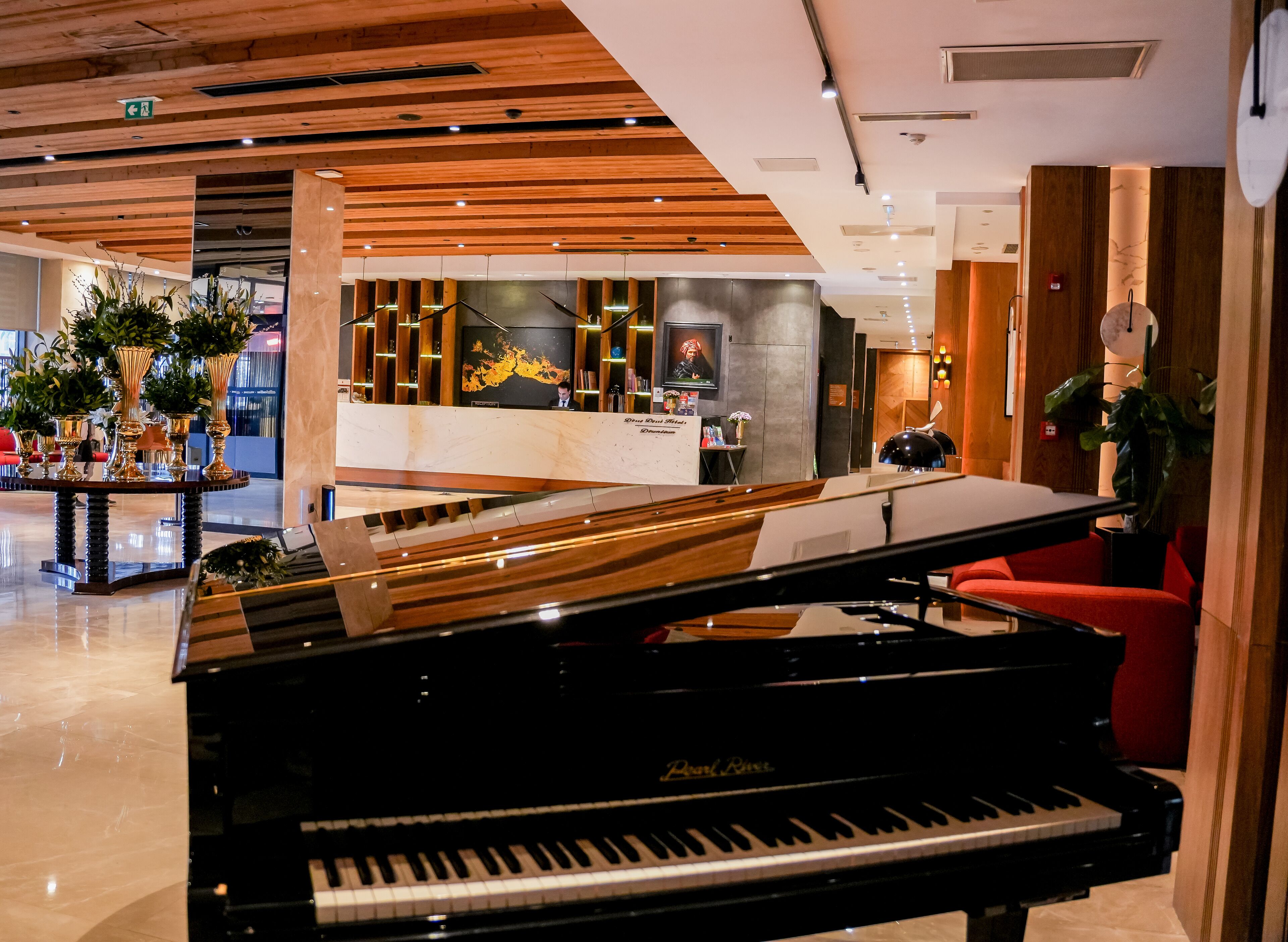 A grand piano in a spacious lobby with a reception desk, wooden ceiling, and modern decor.