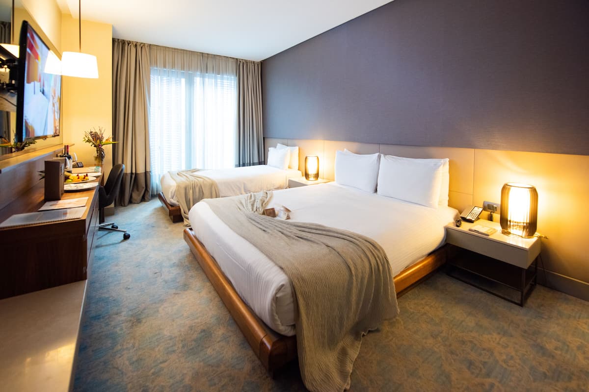 A hotel room with two beds, a desk with a chair, a lamp, and a TV.