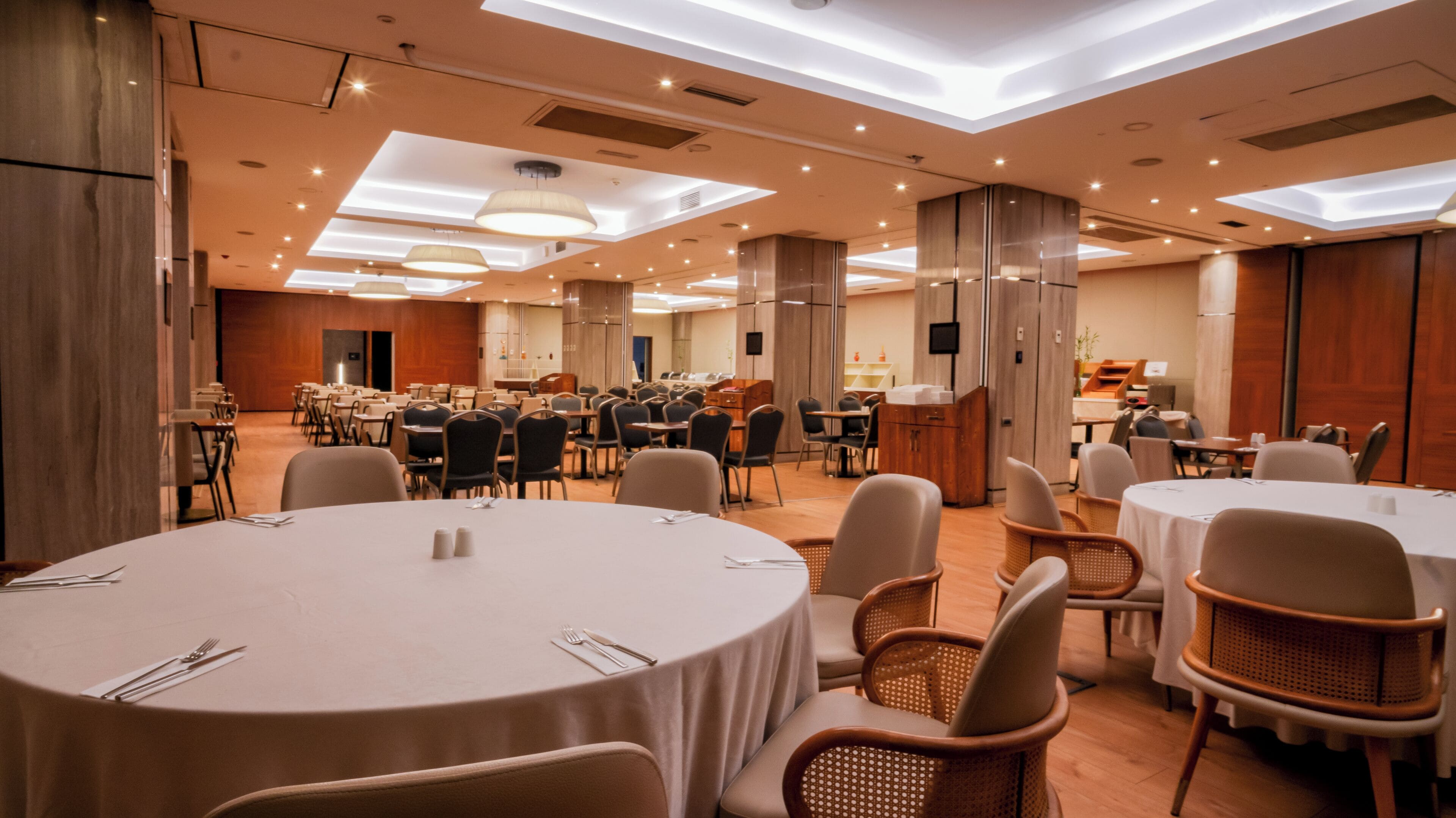 Una amplia sala de conferencias con mesas redondas, sillas y una zona de bufé.