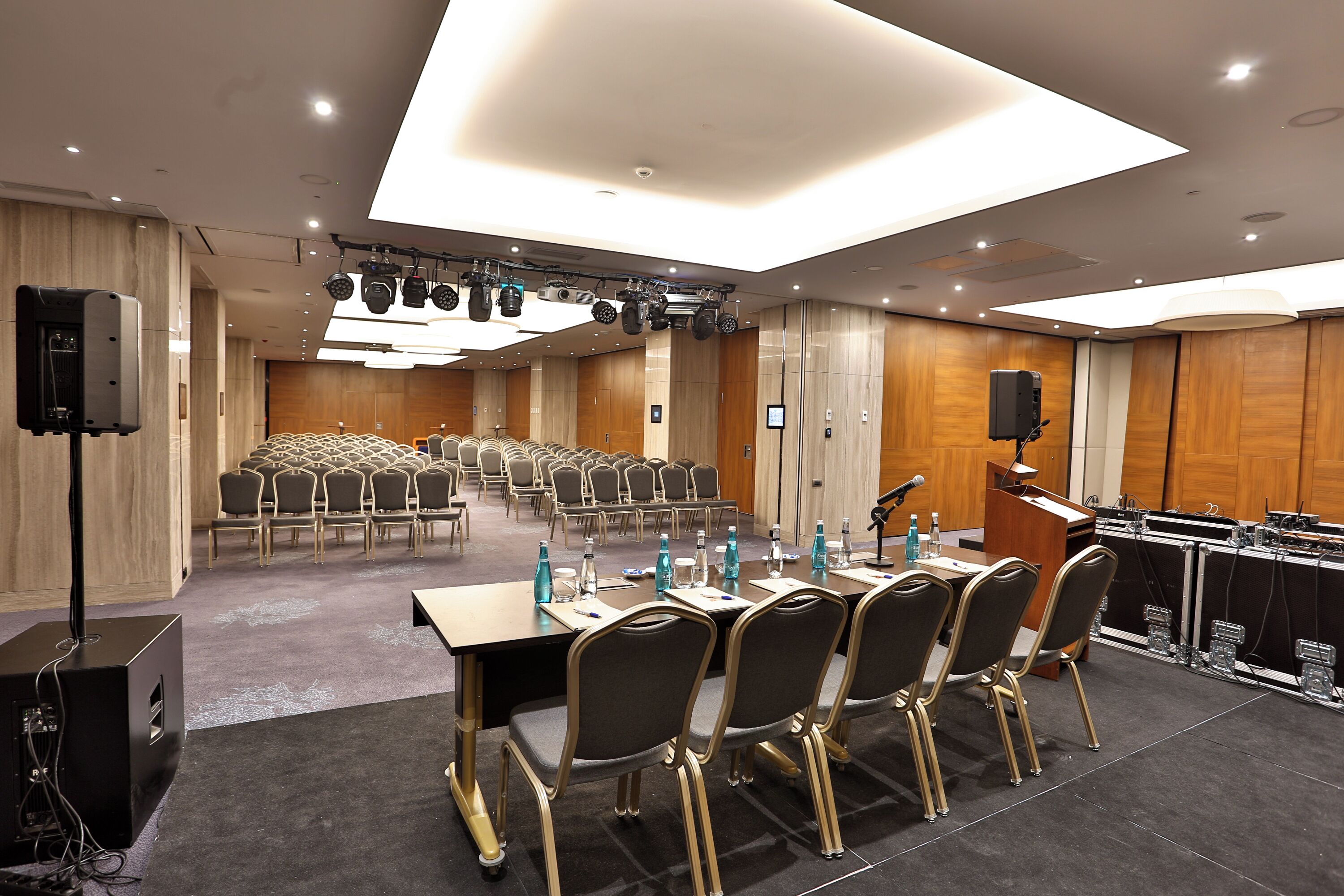 A conference room with rows of chairs, a podium, and a stage with lighting equipment.