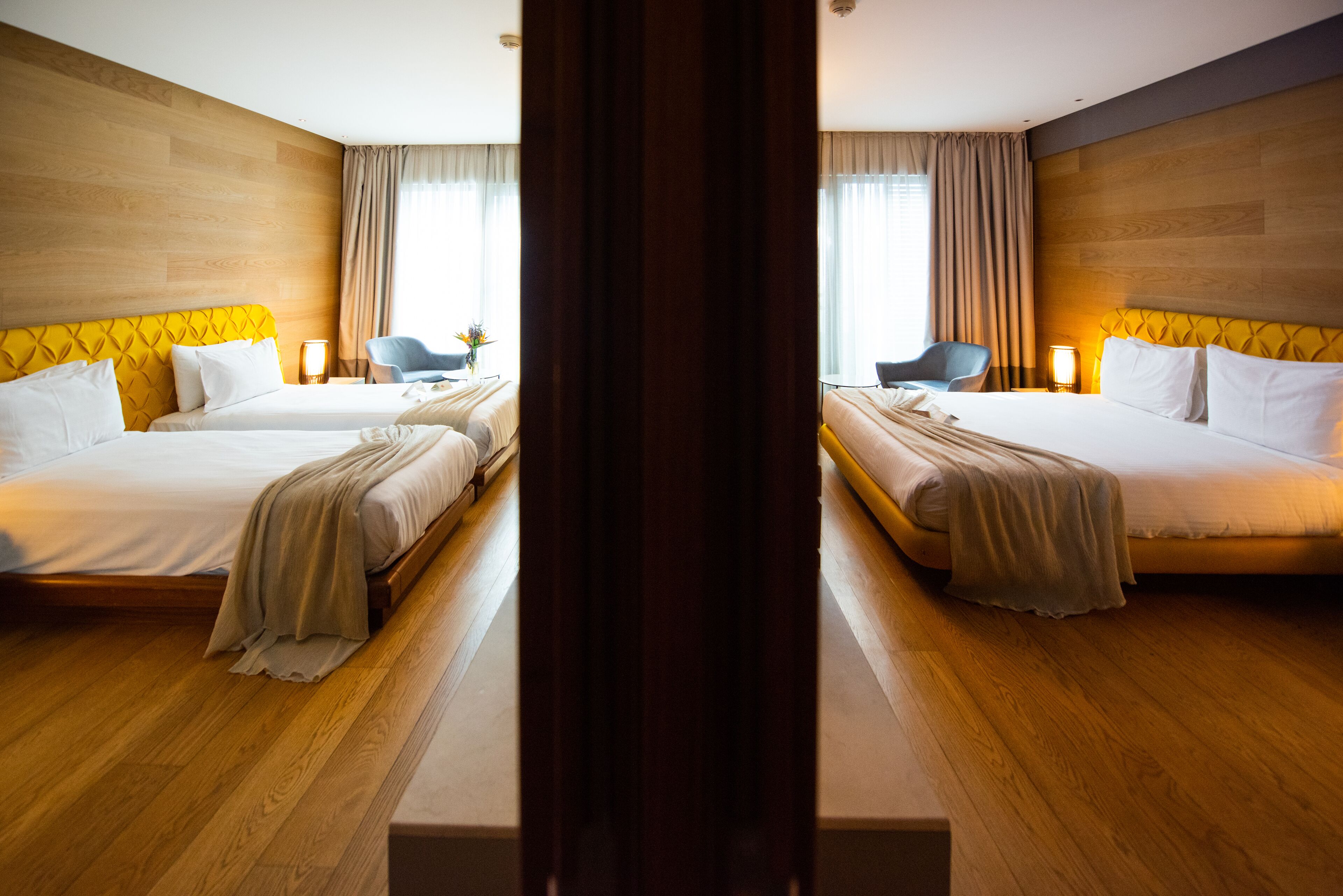 A hotel room with two beds, wooden flooring, and a large window with curtains.