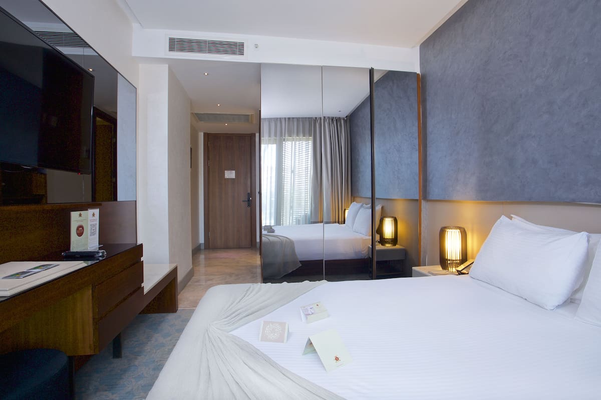 A hotel room with a bed, bedside table, lamp, and a television.