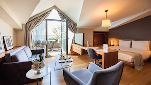 Una habitación de hotel moderna con techo estilo loft, una zona de estar acogedora, una mesa de comedor, un espacio para trabajar y una cama grande.