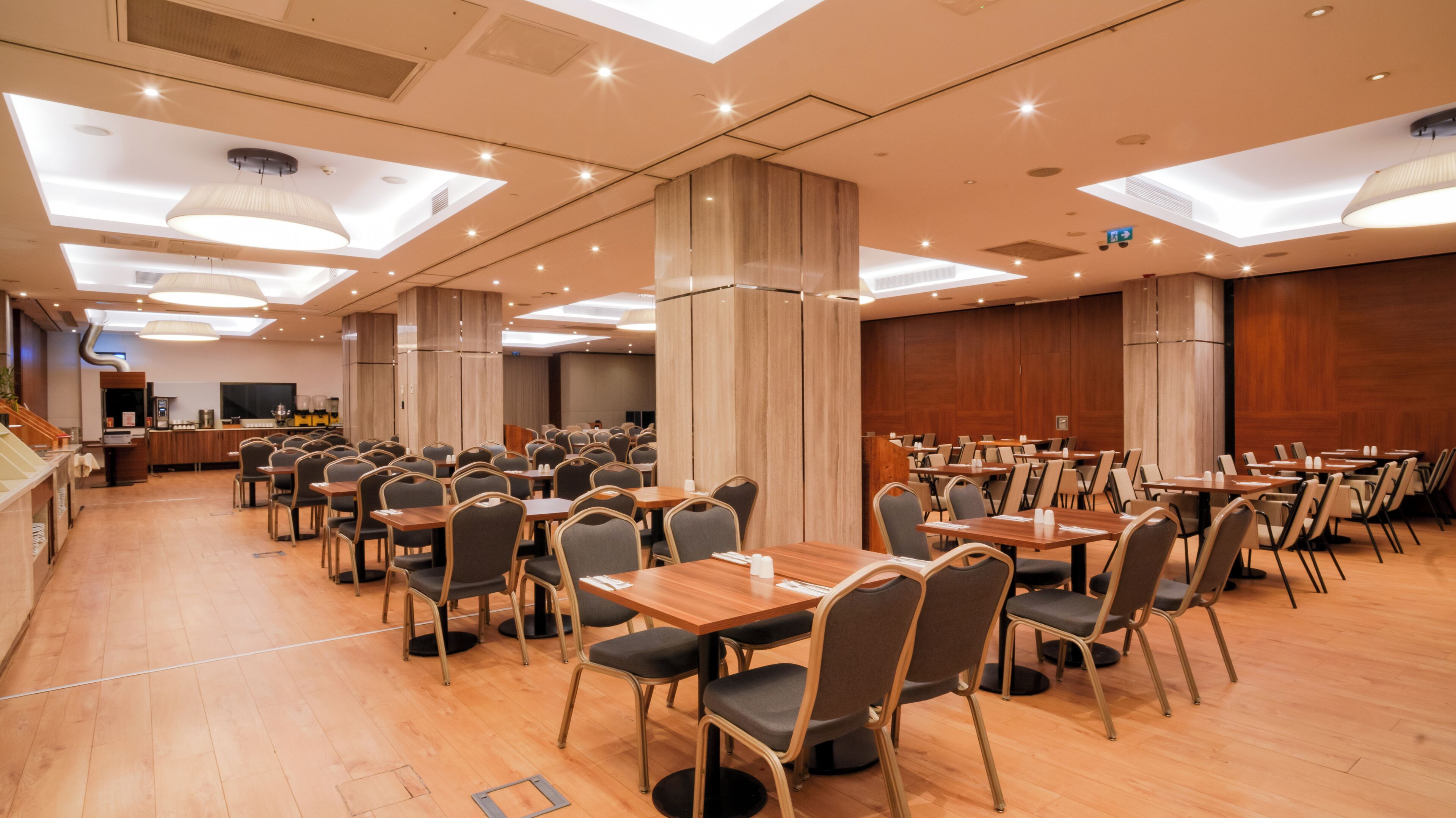 A spacious dining area with multiple tables and chairs, a counter with a beverage station, and a modern ceiling design with recessed lighting.
