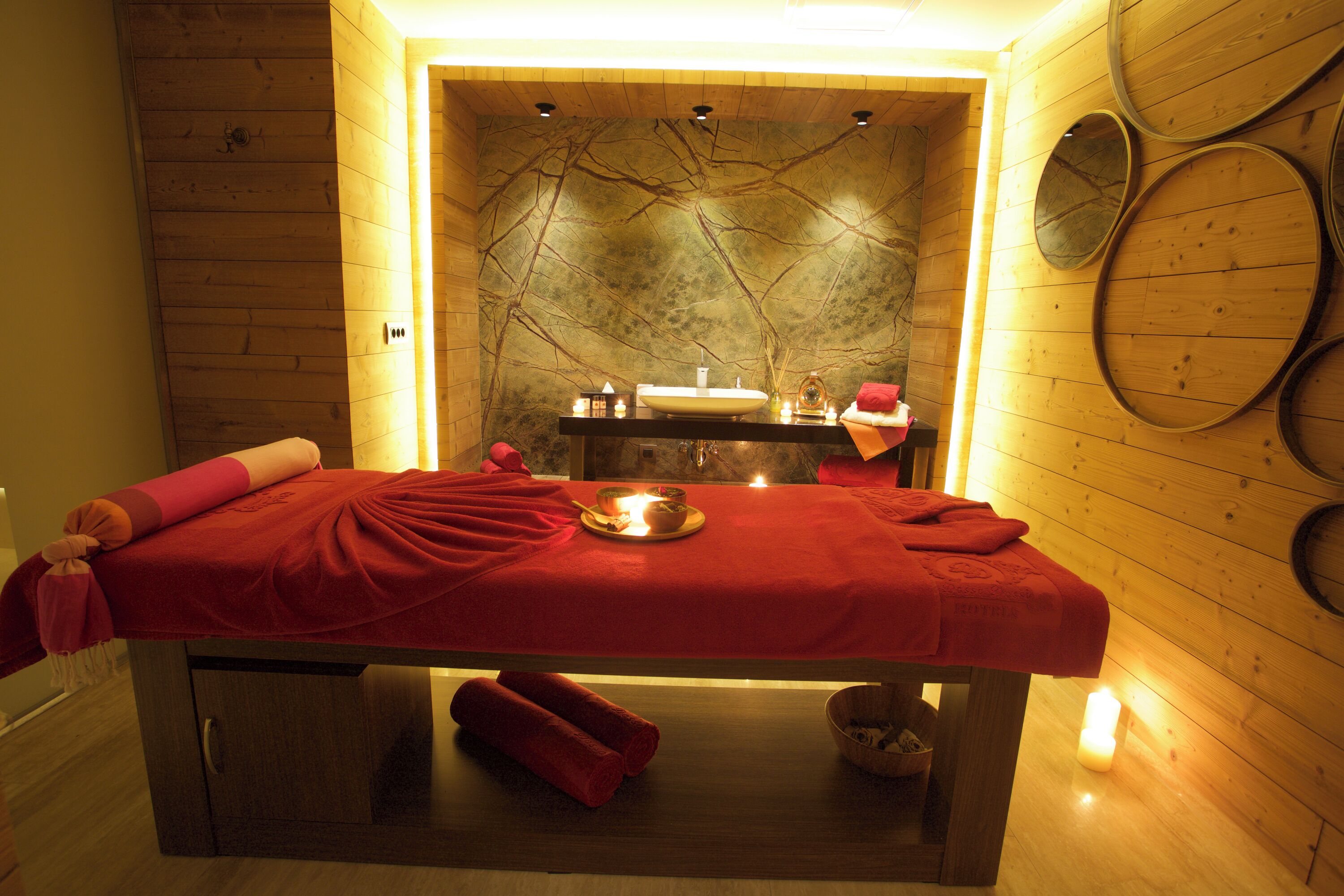 A wooden room with a massage table, candles, and a small sink.