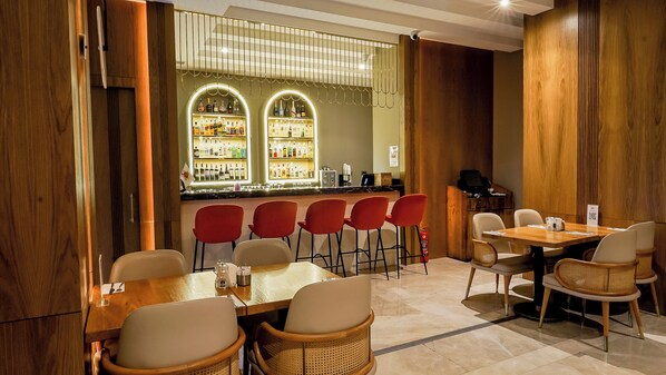 A restaurant with a bar area, red chairs, a wooden table, and a tiled floor.