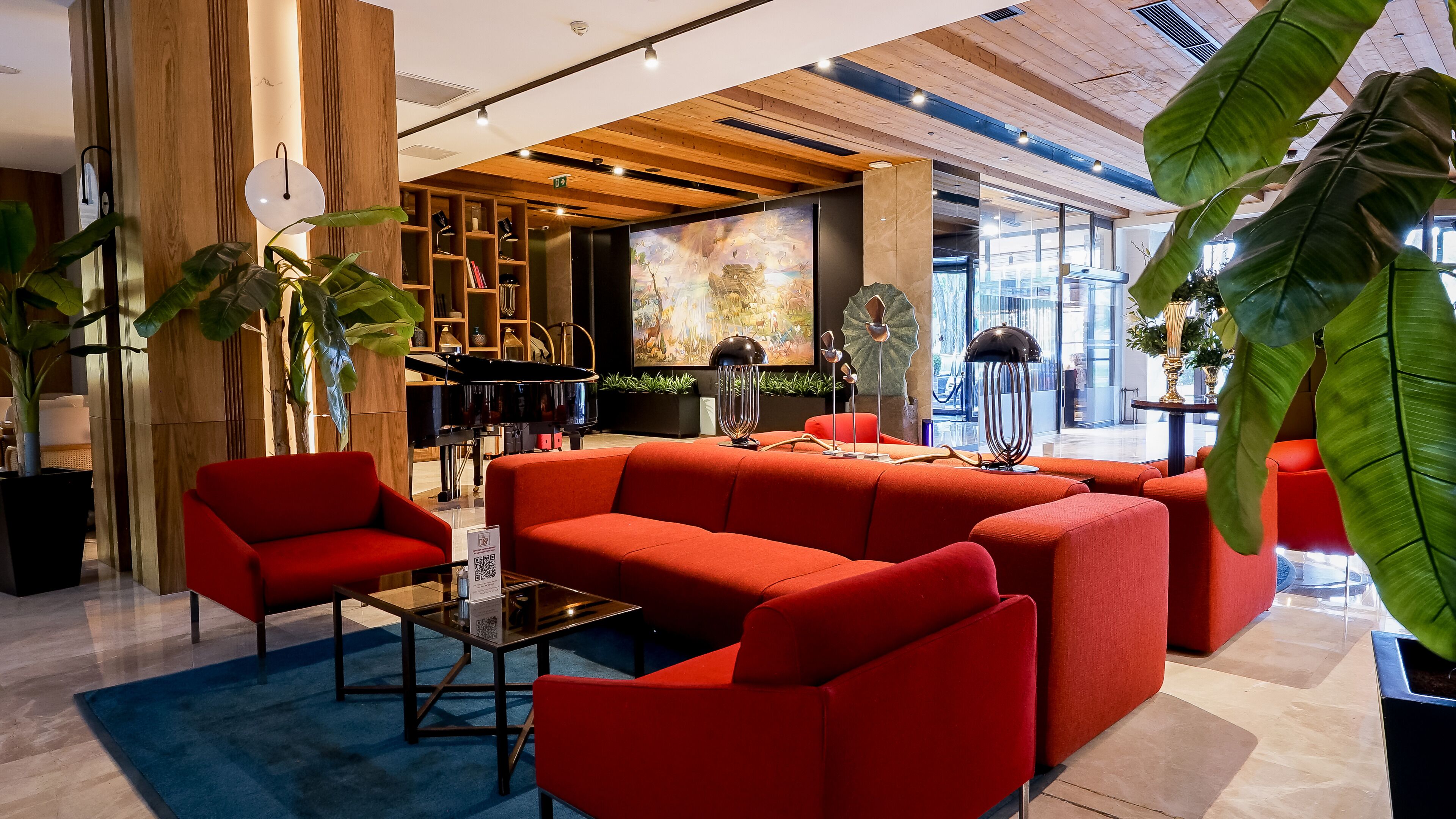 Un área de estar moderna con sofás rojos, una mesa de centro de vidrio y un piano.