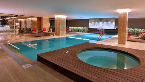 Una piscina interior con hidromasaje, sillones de descanso y un diseño interior moderno.