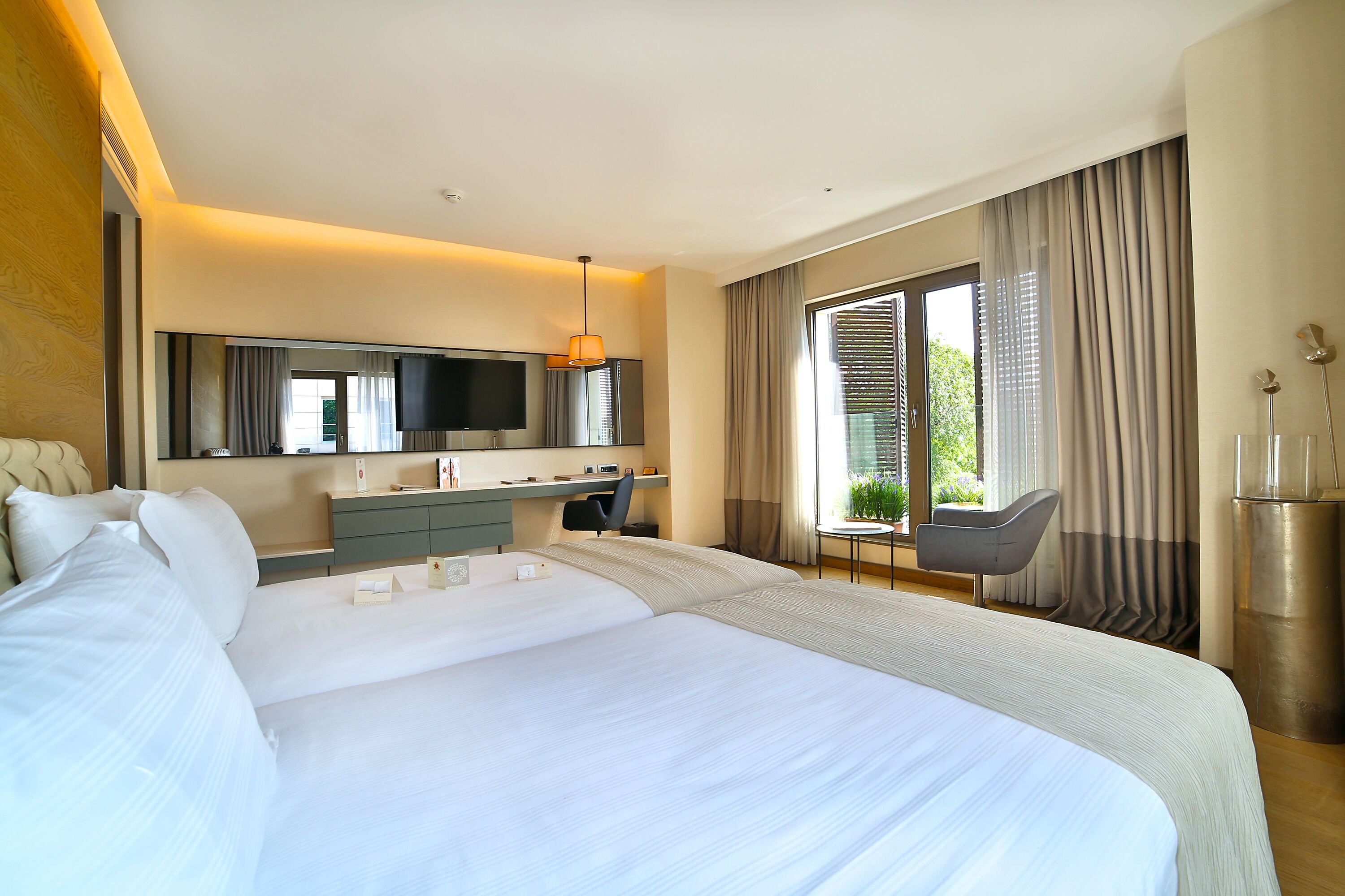 A modern hotel room with a large bed, a desk, a chair, a TV, and a window with curtains.