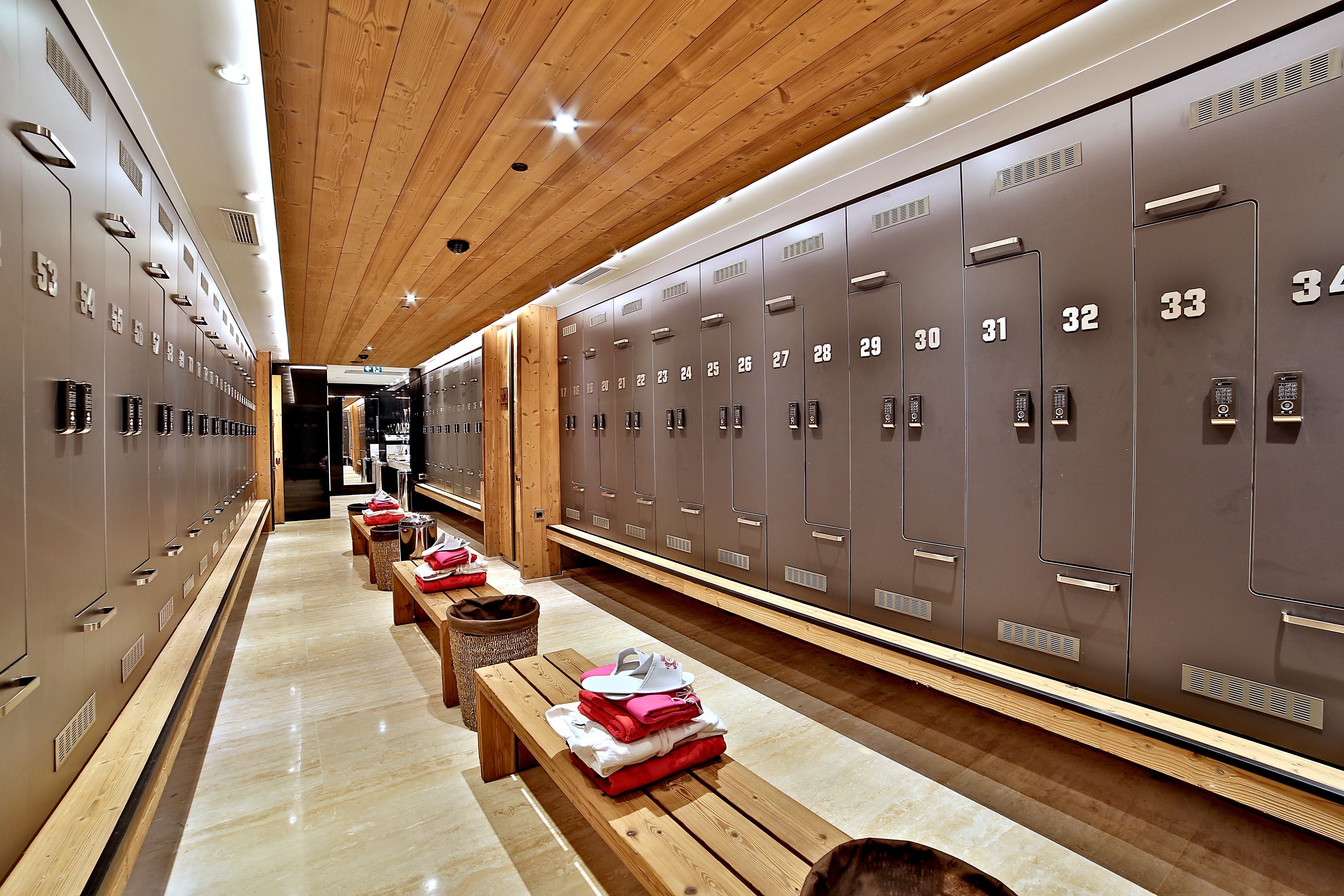 A modern locker room with wooden benches and lockers numbered 1-34.