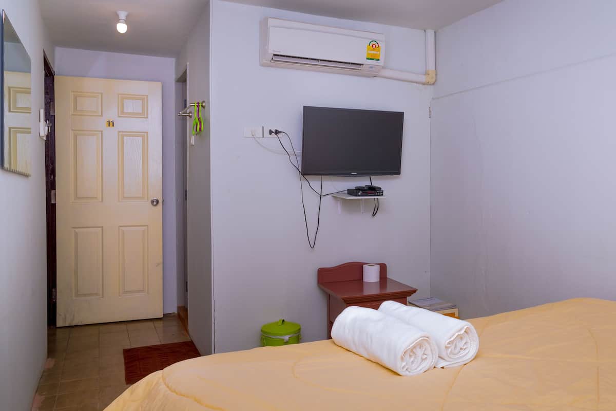 Een hotelkamer met een bed, een aan de muur bevestigde televisie, een kleintje tafeltje en een deur.
