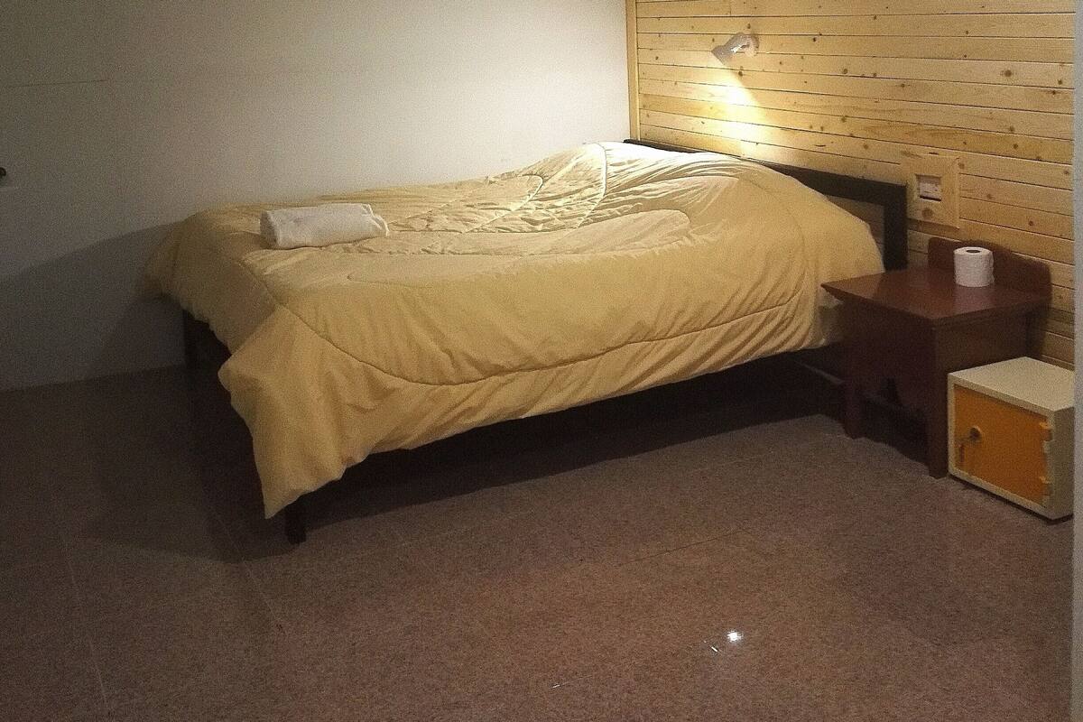 Een slaapkamer met een bed, nachtkastje, lamp en een klein kastje.