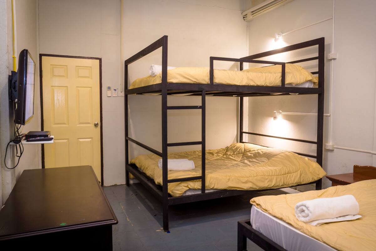 Een studentenkamer met stapelbedden, een bureau en een aan de muur bevestigde televisie.
